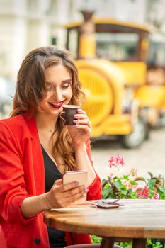 Tourist young caucasian woman in red jacket with coffee cup at the table in cafe outdoors