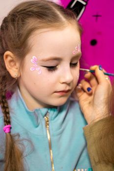 childrens makeup face paint drawings Girls face painting. Little girl having face painted on birthday party. closed eyes. High quality photo