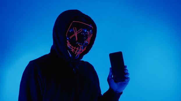 Digital security Concept. Anonymous hacker with mask holding smartphone hacked. Personal and Cyber data security in mobile phone stolen by man in mask. Represent digital privacy protection concept.