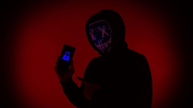 Digital security Concept. Anonymous hacker with mask holding smartphone hacked. Personal and Cyber data security in mobile phone stolen by man in mask. Represent digital privacy protection concept.