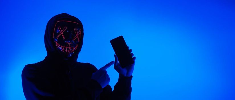 Digital security Concept. Anonymous hacker with mask holding smartphone hacked. Personal and Cyber data security in mobile phone stolen by man in mask. Represent digital privacy protection concept.