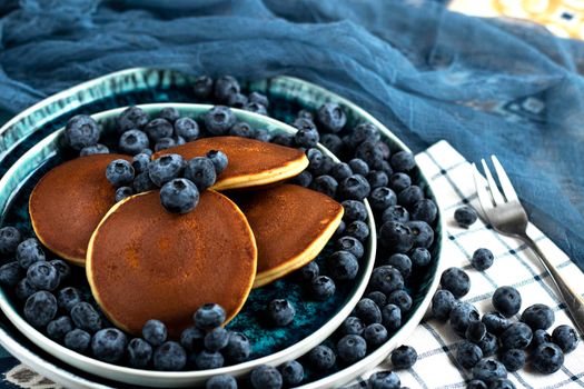 selective focus. pancakes with blueberries on a blue plate. Lots of fresh blueberries scattered around. Delicious dessert with berries for breakfast. High quality photo