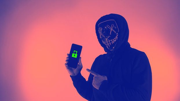 Digital security Concept. Anonymous hacker with mask holding smartphone hacked. Personal and Cyber data security in mobile phone stolen by man in mask. Represent digital privacy protection concept.