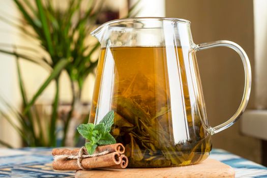 selective focus. Green tea in a teapot with cinnamon sticks and fresh mint. Hot tea in a glass teapot in the kitchen. Large tea leaves. drink with mint and cinnamon.