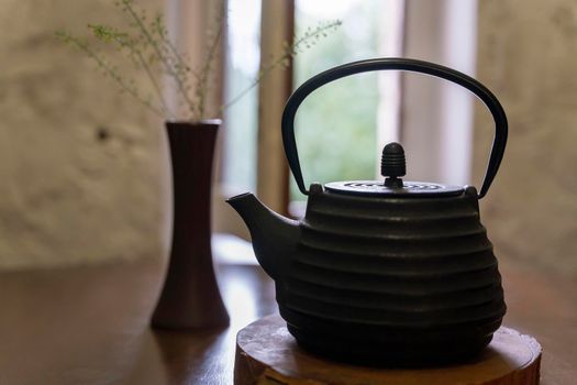 cast-iron kettle on a wooden stand on the restaurant table against the background of the window. time to drink tea