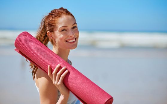 Yoga is about showing up to your mat. a young woman posing with her yoga mat on the beach