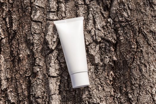 Organic cosmetic cream in tube on a tree bark natural background. Beauty product packaging mockup. Cream bottle, lotion, mousse, shampoo for skincare routine. Top view, copy space, closeup.