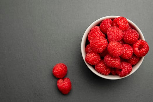 Fresh juicy raspberries in a small black plate. Bright red crimson close-up. Summer berry picking time. Healthy organic fruits for kids.