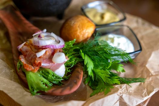 Meat on a wooden spoon plate served with herbs and sauces on a wooden plate on the table in a restaurant. Close-up, selective focusing