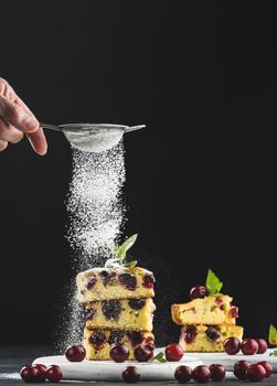 Baked sponge cake with cherries sprinkled with powdered sugar, black background