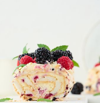 Baked meringue roll with cream and fresh fruits on a white wooden board, delicious dessert