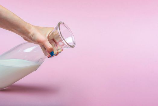 A jug of milk on a pink background in a woman's hand. Milk in a glass bottle. Space for text, large banner