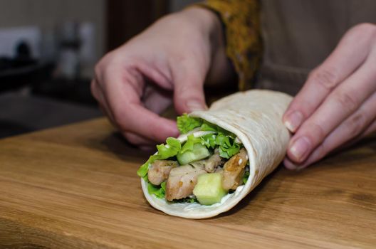 Delicious lavash rolls with fried chicken and vegetables on a wooden cutting board. Cooking process, close-up