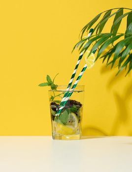 Transparent glass with lemonade, mint leaves, lemon slices and blackberries in the middle