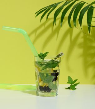 Transparent glass with lemonade, mint leaves, lemon slices and blackberries in the middle