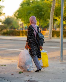 Islamic woman walking with rubbish. Rear view of a muslim or Arab young girl carrying garbage bags on the street