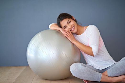 The ball that gets me on the ball. a sporty young woman leaning on a pilates ball against a grey background