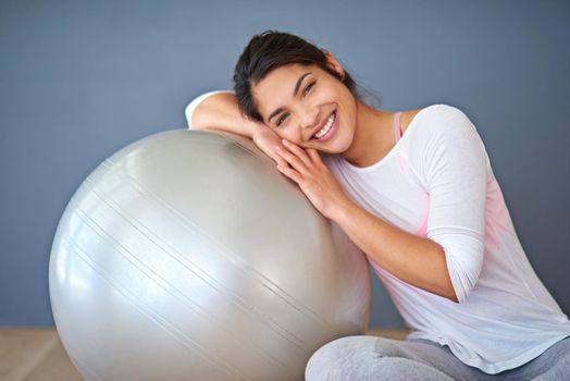 Take time to do what makes your soul happy. a sporty young woman leaning on a pilates ball against a grey background