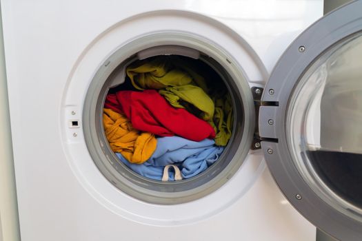 Washing machine with open door and bright colored clothes inside, close-up. view