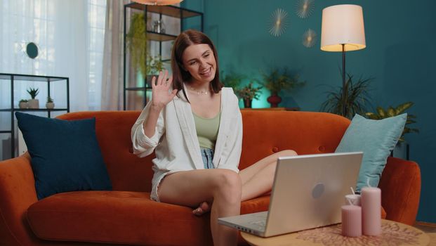 Portrait of caucasian girl sitting on couch, looking at camera, making video webcam conference call with friends or family, enjoying pleasant conversation. Young woman laughing, waving hello at home