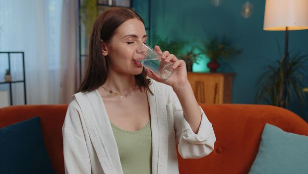 Portrait of thirsty lovely girl sitting indoors holding glass of natural aqua make sips drinking still water preventing dehydration. Woman with good life habits, healthy slimming, weight loss concept