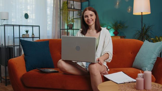 Girl accountant working with financial graph documents, calculate taxes for charts and graph reports of home income on couch. Young businesswoman working on laptop computer, planning expenses budget