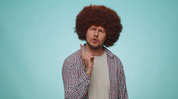 Displeased man shakes finger and saying no, be careful, scolding and giving advice to avoid danger mistake, disapproval, disagree, warning sign. Young guy isolated alone on blue studio wall background