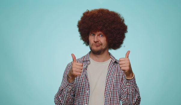 Great job, nice. Cheerful positive happy bearded man in shirt showing thumbs up and nodding in approval, successful good work. Young stylish one guy on blue studio background. People sincere emotions