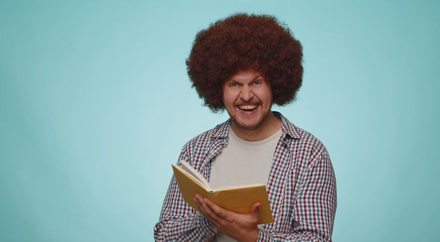 Happy smiling bearded man reading funny interesting fairytale story book, leisure hobby, knowledge wisdom, education, learning, study, wow. Young adult guy boy isolated alone on blue studio background