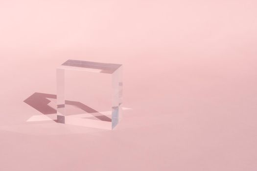 Acrylic block, podium for product presentation. Glass transparent cube with sun reflection, geometric stand for cosmetic, light and shadow on pink. Physics refraction effect, translucent prism.