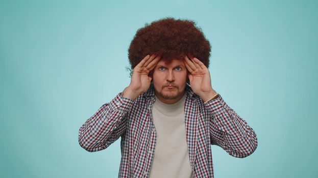 Nosy curious man closing eyes with hand and spying through fingers, hiding and peeping, binocular gesture, exploring way, seeking something in distance. Young adult guy boy on blue studio background