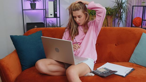 Girl accountant working with financial graph documents, calculate taxes for charts and graph reports of home income on couch. Young businesswoman working on laptop computer, planning expenses budget