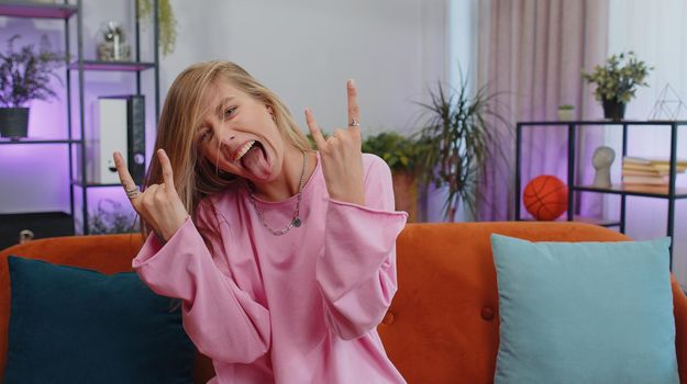 Overjoyed delighted caucasian adult girl showing rock n roll gesture by hands, cool sign, shouting yeah with crazy expression, dancing, emotionally rejoicing in success. Young woman at home apartment