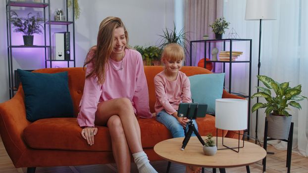 Blogger mother and child kid daughter sit at home living room enjoy listening music, dancing, recording video content for social media. Family enjoy selfie filming by internet network wifi connection