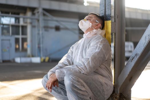 Despair healthcare worker in white covid protective overalls.Tired Male caucasian doctor grabs his head cower in depression during coronavirus pandemic Paramedic overworked cry covered face with hands