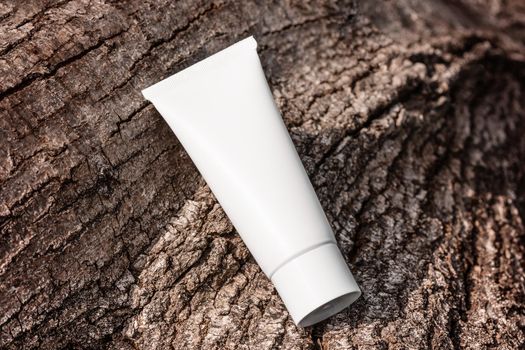 Hand cream, moisturizer, lotion in white plastic tube on tree bark top view. Anti-age product template, luxury body care and organic science concept. Cosmetics packaging with natural ingredients