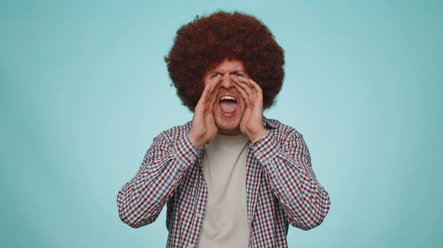 Expressive man holding hands near mouth loudly screaming, shouting, yelling, announces discounts sale Hurry up, welcomes someone hello. Young adult guy isolated alone on blue studio wall background