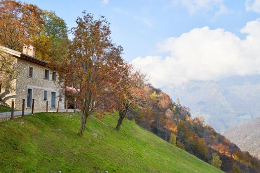 View on house on the mountain side, picturesque Alps autumn landscape, mountain hills in Lombardy, Italy. Tourist adventure, colorful autumn scene