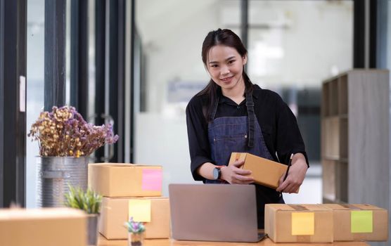 Young attractive asian woman owner startup business look at camera work happy with box at home prepare parcel delivery in sme