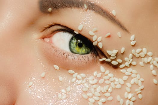 Open, green eye of a woman with white sesame seeds on the eyelid, around the eye. Expressive look