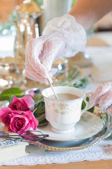 English retro still life and a woman's hand in a white lace glove stirring coffee with milk in an elegant cup from Chinese porcelain, light and airy early morning mood. High quality photo