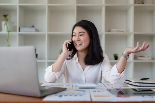 Young asian business woman smiling and talking on mobile phone at office.