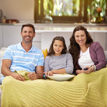 Family movie night. a family sitting on their living room sofa watching a movie and eating popcorn