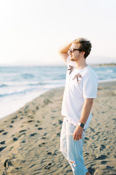 Man in sunglasses stands on the beach straightening his hair in the wind. High quality photo