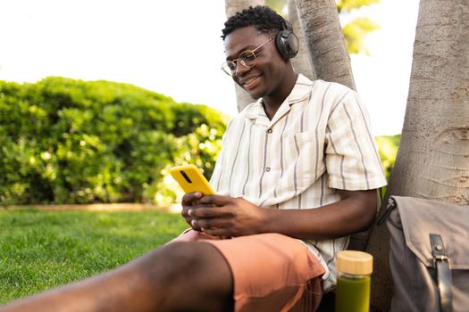 African american man relaxing outdoors listening to music using phone and headphones Black teen college student relaxing on campus. Copy space. Leisure concept.