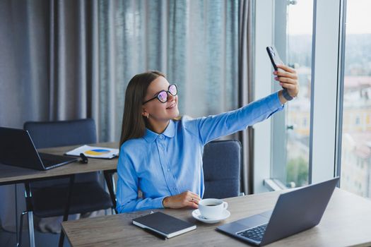 Smart female employee with netbook looking at camera during mobile call, successful freelancer in jacket talking on phone via app