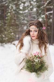 Beautiful bride in a white dress with a bouquet in a snow-covered winter forest. Portrait of the bride in nature.