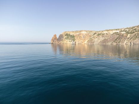 Sea landscape with rocky coastline on sunset time with cloudy sky. Yachts in the Sea on a background of rocky shores. The concept of perfect place for summer travel and rest.