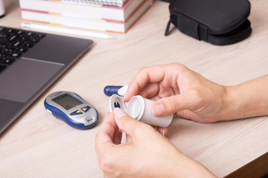 Female hands with a glucometer at the desk. The lifestyle of a person with diabetes, measuring the level of glucose in the blood.