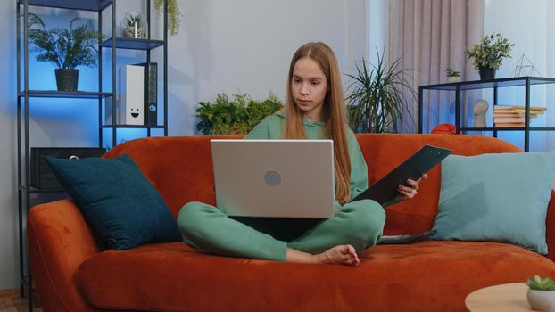 Girl accountant working with financial graph documents, calculate taxes for charts and graph reports of home income on couch. Young businesswoman working on laptop computer, planning expenses budget